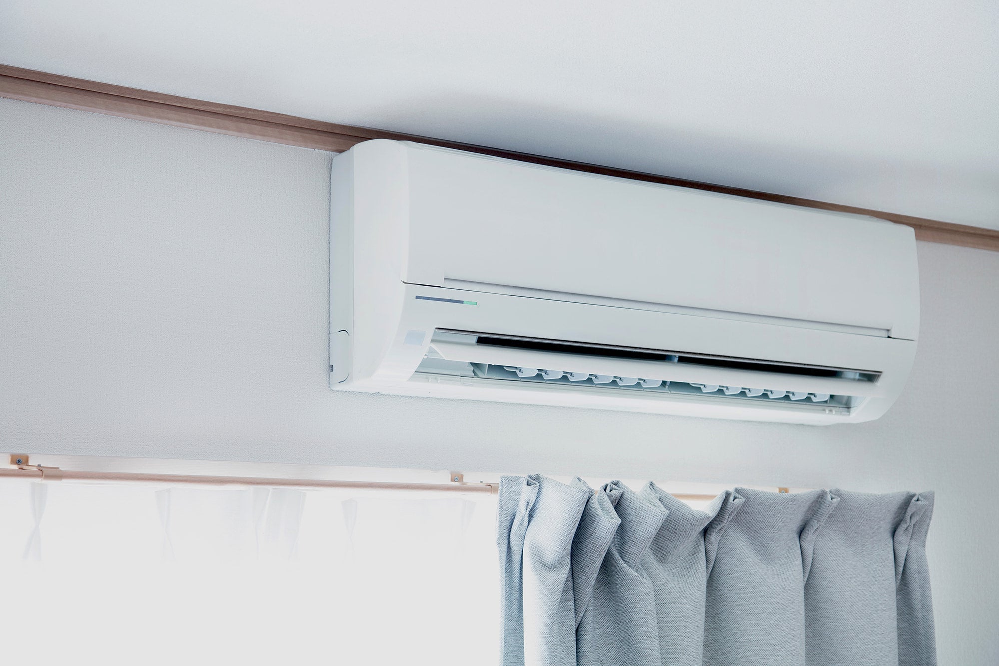 White air conditioner mounted on a wall with curtains below
