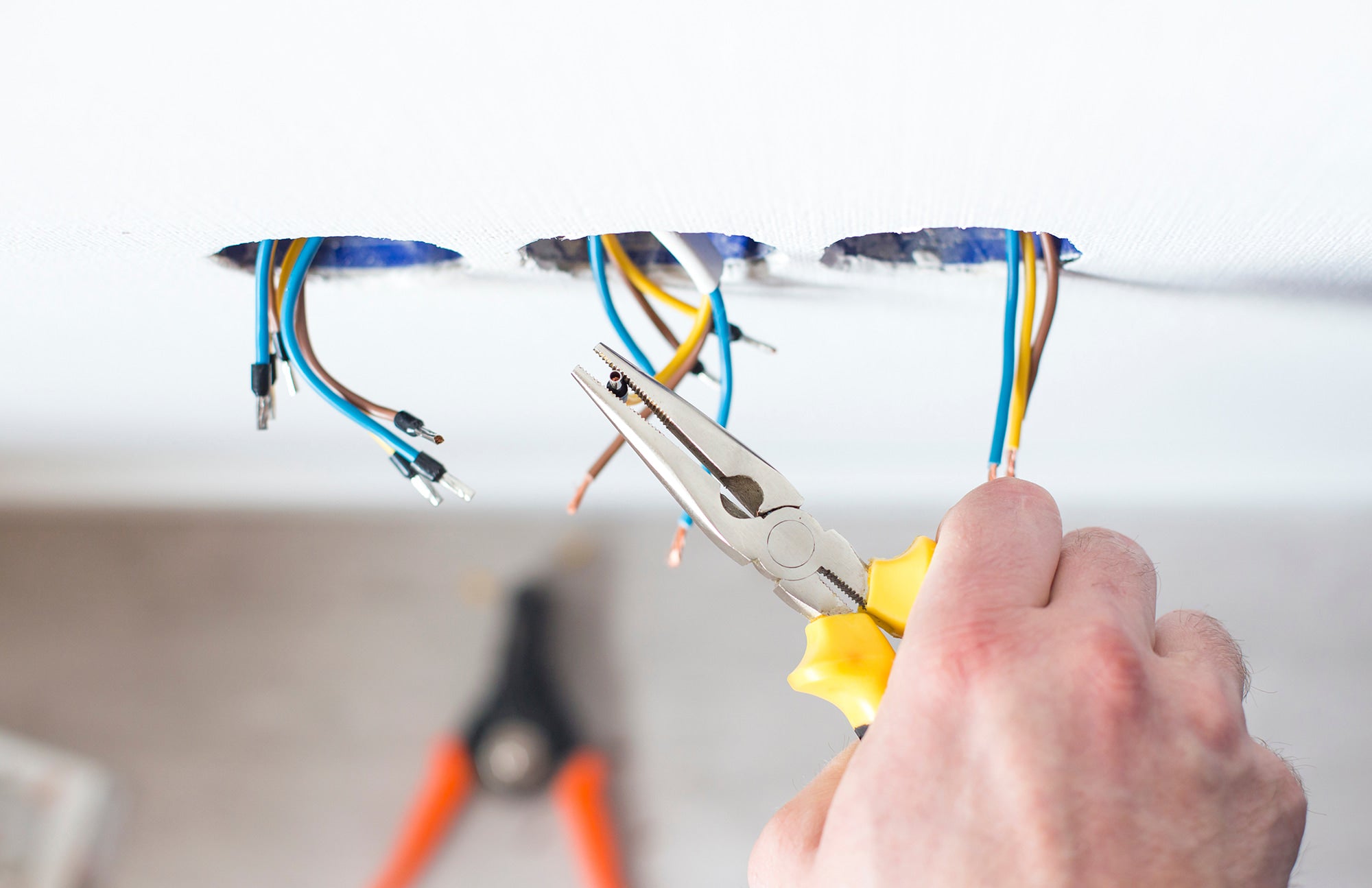 Person using pliers to work with electrical wires on a white surface.
