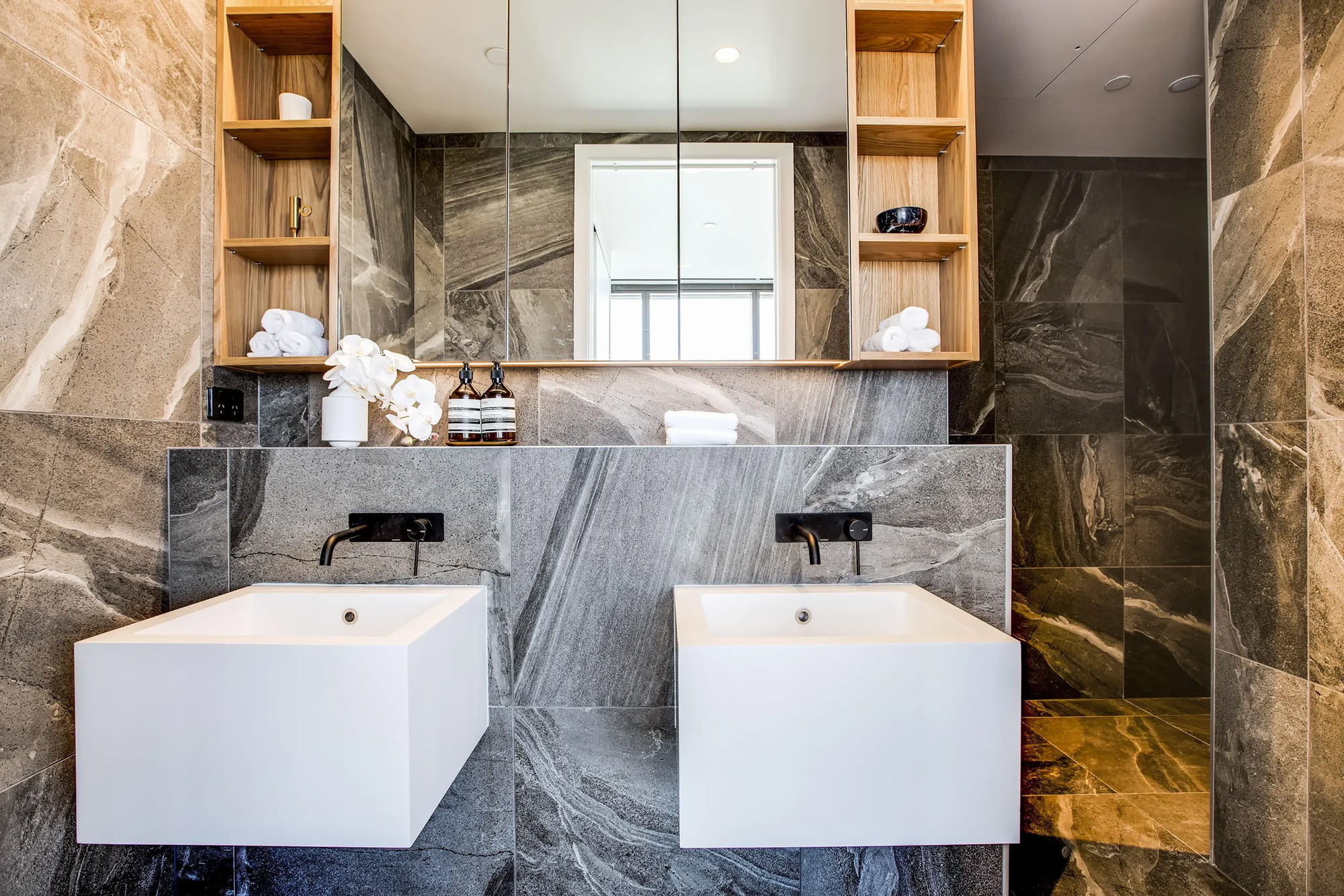 Modern bathroom with marble walls, double sink, and wooden shelves.